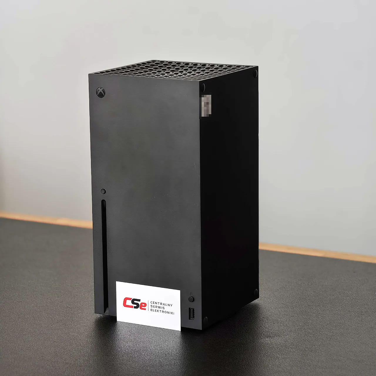 Xbox Series X stojący pionowo na stole serwisowym z wizytówką CSE Poland